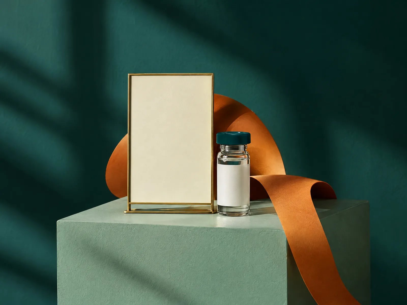 Blank cream billboard in a brass frame on a pale teal plinth beside a teal-cap vial and an amber ribbon